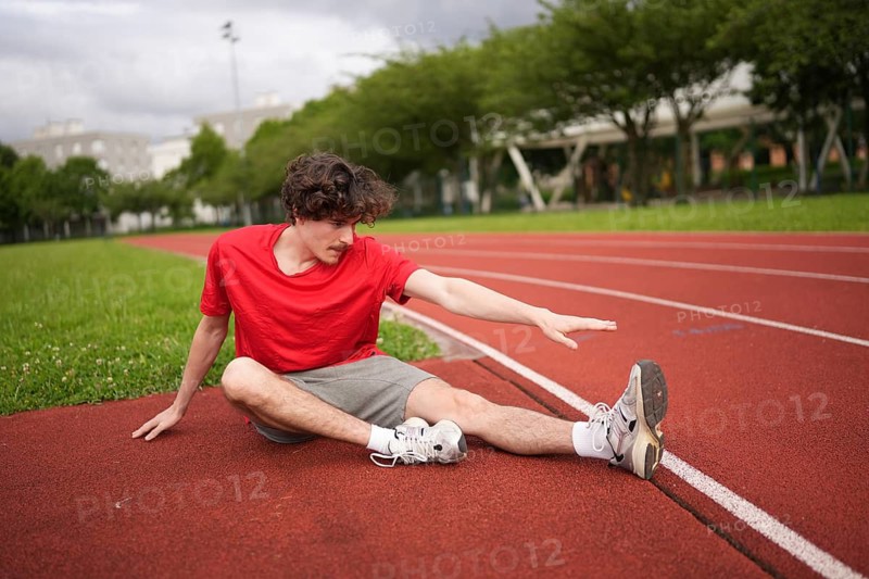 Young caucasian man stretching legs before running in an outdoor running track