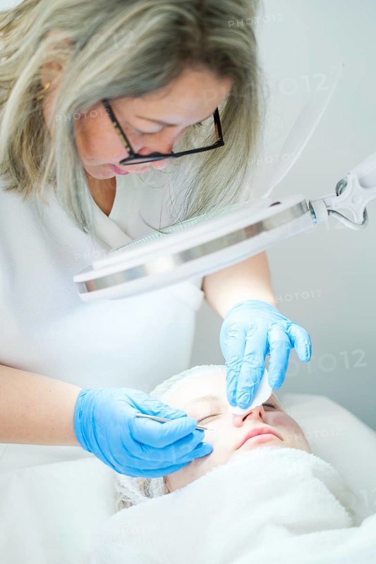 Esthetician cosmetologist uses a metal extractor tool for deep pore cleansing, removing blackheads effectively in a spa setting