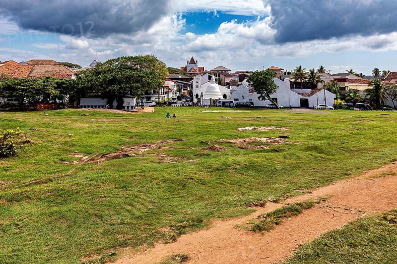 Wide meadow with a view of a small town and a church under a cloudy sky, the historic downtown of Galle in Sri Lanka
