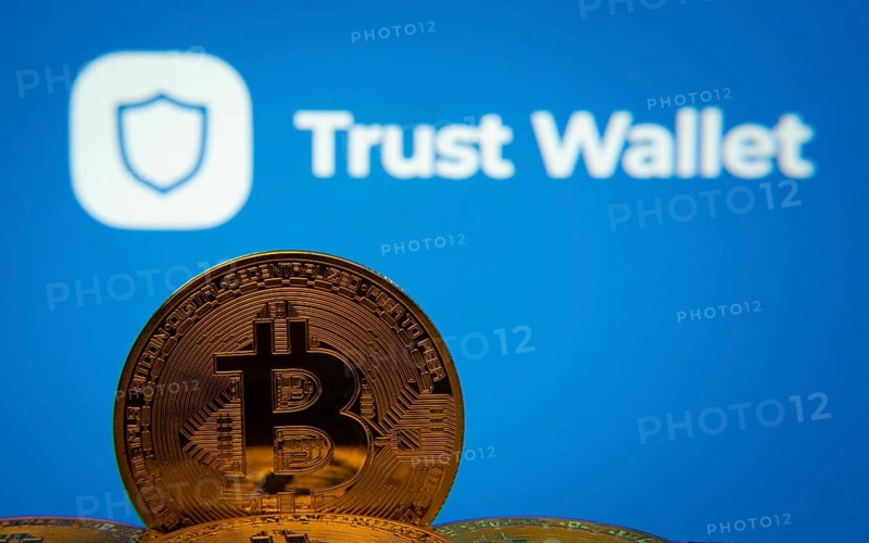 Dhaka, Bangladesh- 30 Sep 2025: Close-up of Bitcoin coins with the Trust Wallet logo visible on a screen in the background