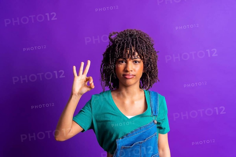 Studio portrait capturing a young woman making an okay gesture with her hand against a vibrant purple backdrop, radiating positivity