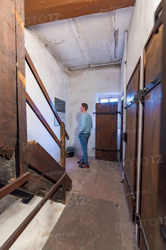 A man looks at a sign in a room with wooden stairs and antique doors, Prison Museum, Der Lange, Calw, Black Forest, Germany