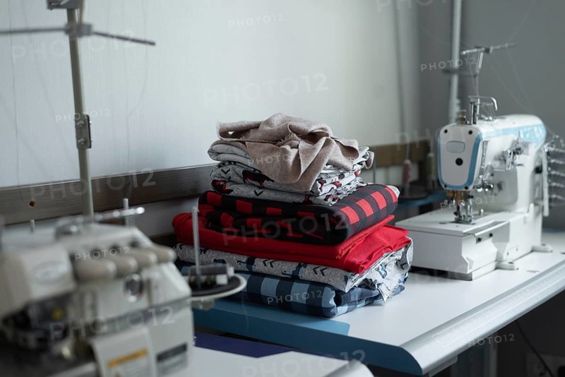 A sewing workshop showcasing colorful fabric stacks on a worktable, with a sewing machine in the background. The image captures the essence of a creative sewing space