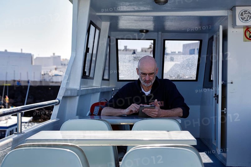 Tourist sitting on an excursion boat and reading a tablet, Orzola, Lanzarote, Spain