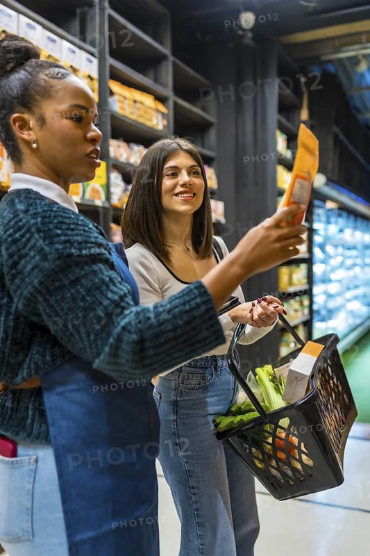 Saleswoman assisting a customer in selecting fresh groceries for a shopping basket, highlighting a variety of healthy and organic options