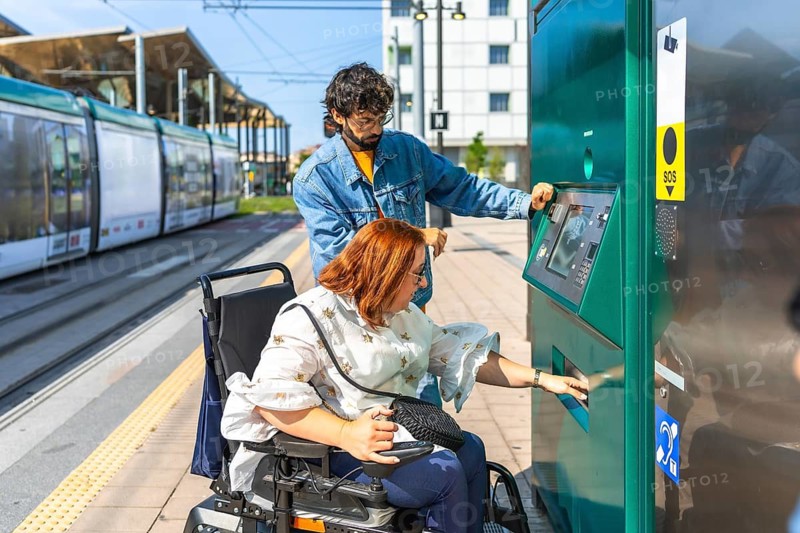 Young redhead woman with her male friend buying a ticket at automatic ticket machine at a tram station