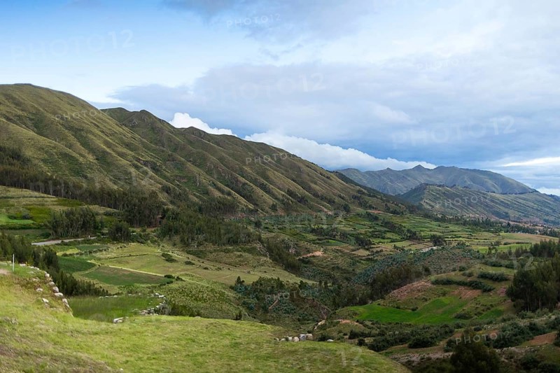 A breathtaking panoramic view of the verdant Andean landscapes near Cusco in Peru, showcasing rolling hills, cultivated fields, and scattered cloud formations