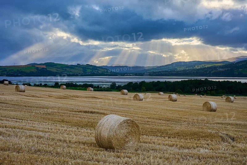 Straw bales in a field with dramatic sky and rays of light over a lake and mountains, Dingwall, Cromarty Firth, Scotland, United Kingdom, Great Britain