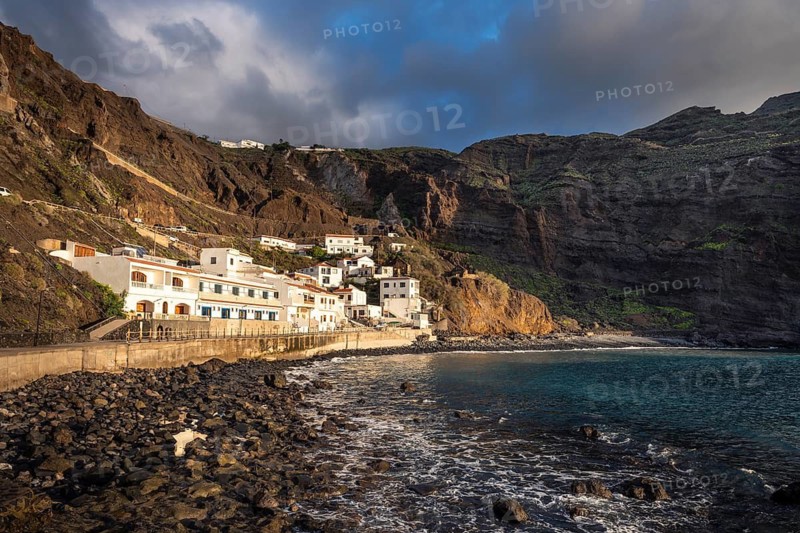 View of some of the houses belonging to Alojera and the Playa de Alojera beach. Steep coast and mountains in the background. Alojera, La Gomera, Canary Islands, Spain