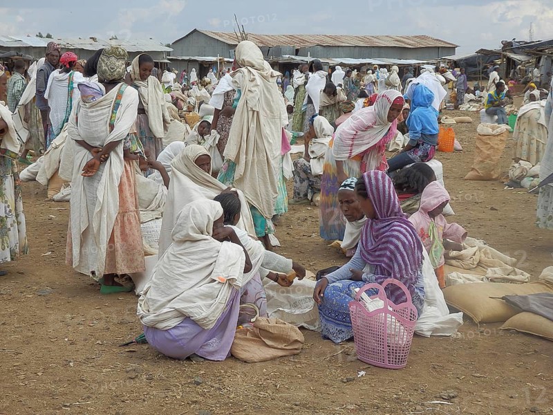 A lively market with lots of people in traditional clothes standing and interacting in groups, Ethiopia