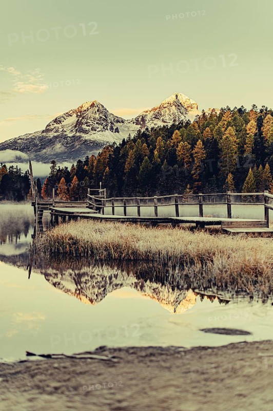 Lake Staz near Sankt Moritz in the Engadin in Switzerland. Morning atmosphere with fog in autumn. Water reflection and snow-covered mountains in the background