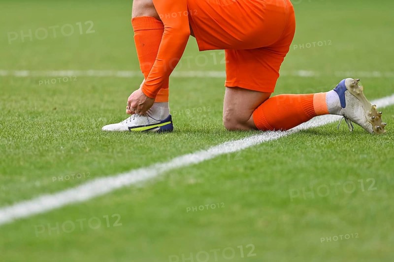 The football player ties shoelaces in his shoe on the turf of the pitch in Lubin, Poland