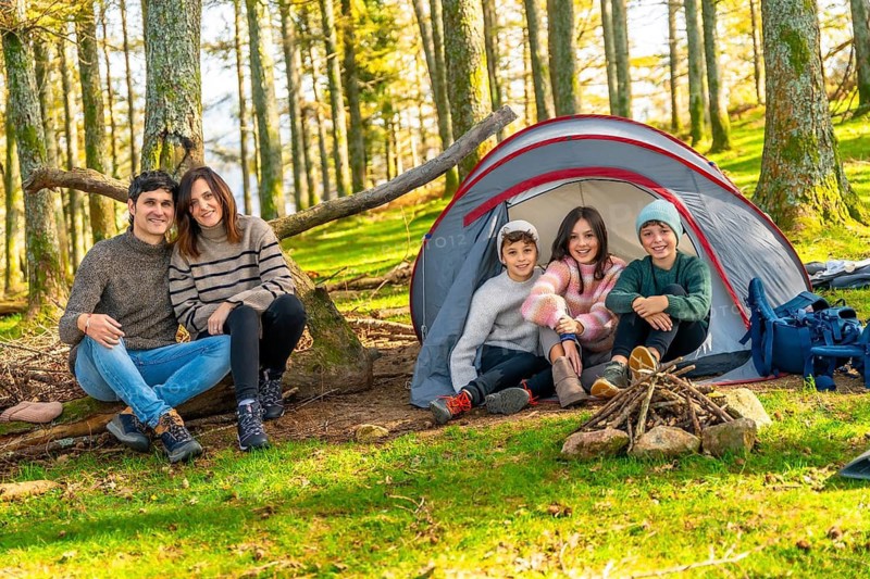 Full length photo of a happy caucasian family sitting next to bonfire enjoying weekend in the forest
