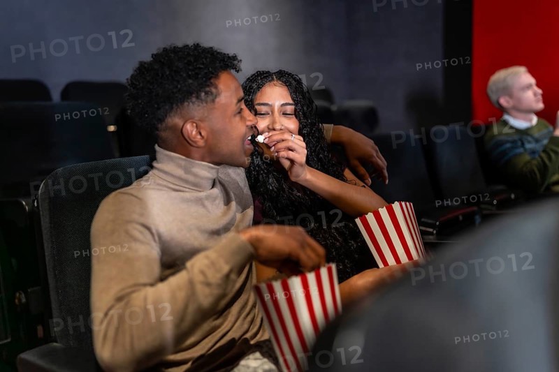 Young couple enjoys a movie date, sharing popcorn and affection while watching a film in a cinema