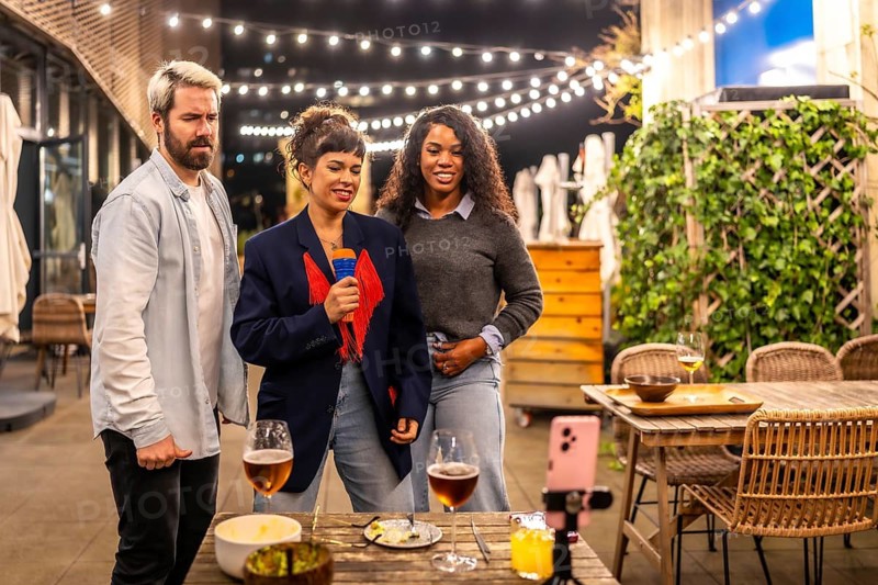 Multi-ethnic male and females friends singing karaoke after dinner in the terrace of a night bar