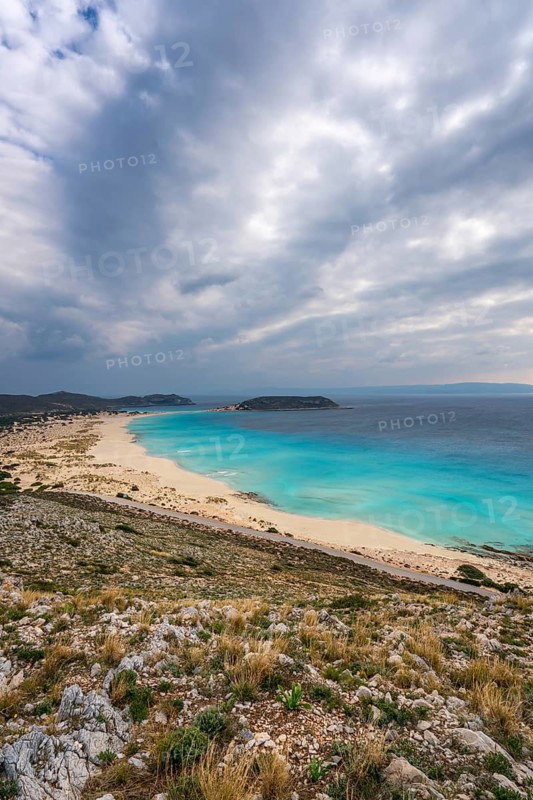 A panoramic view of Simos Beach on Elafonisos Island, Greece, showcasing pristine turquoise waters, golden sands, and dramatic skies. A serene coastal destination with stunning scenery