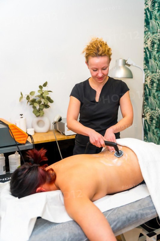 Vertical photo of a therapist using Indiba electric tool for back pain of a patient