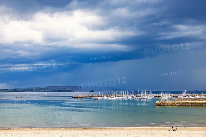 Seascape view at a marina with boats at a pier and a sand beach and a dark storm clouds on the sky, Morgat, Bretagne, Crozon peninsula, France