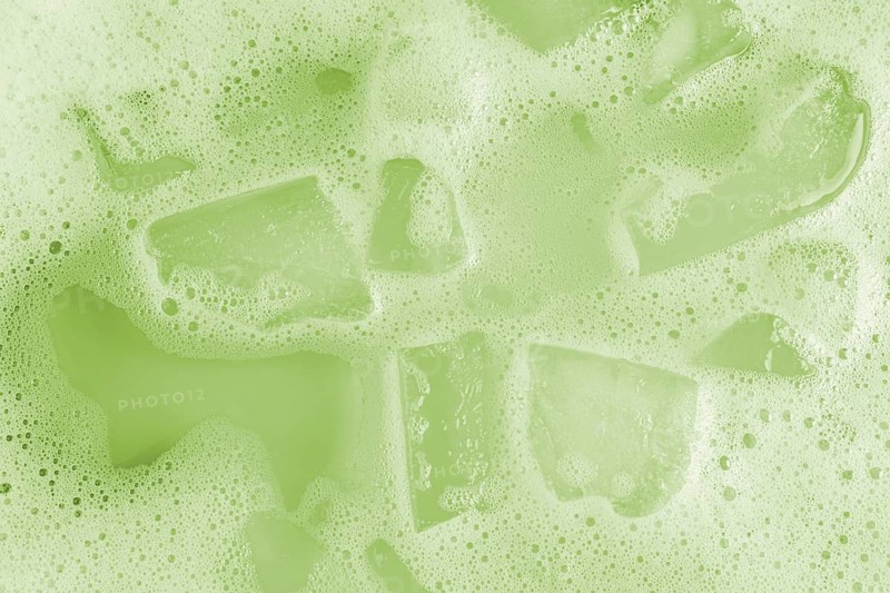 Close-up image of iced cold matcha displaying vibrant green frothy texture and ice cubes. The refreshing beverage's surface bubbles capture a sense of freshness and vitality