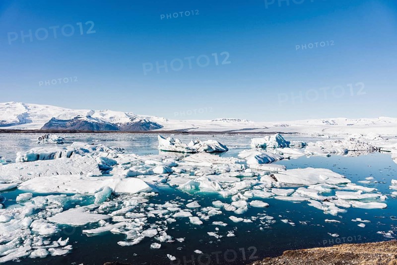 Stunning view of icebergs floating in the serene blue waters of Jokulsarlon glacier lagoon, set against the backdrop of snow-capped mountains in Iceland's breathtaking landscape