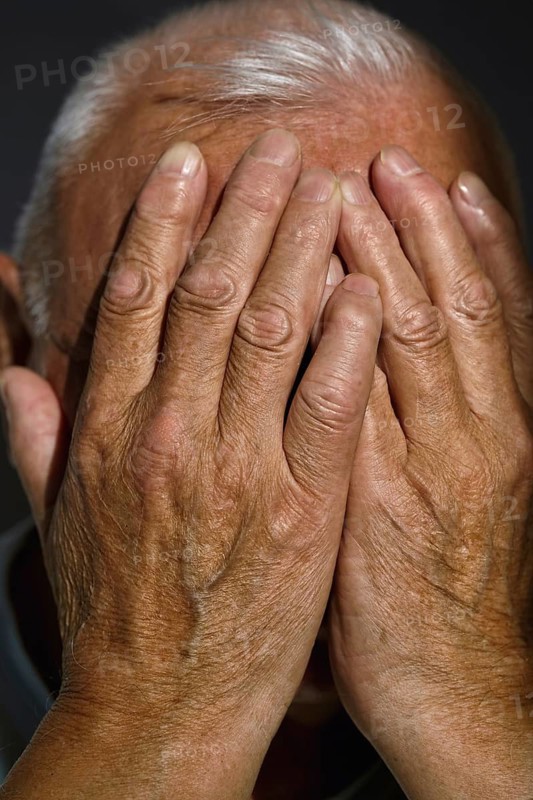Close-up of a senior man covering his face with age-marked hands in a moment of contemplation Captures the texture of mature skin and expressive gesture