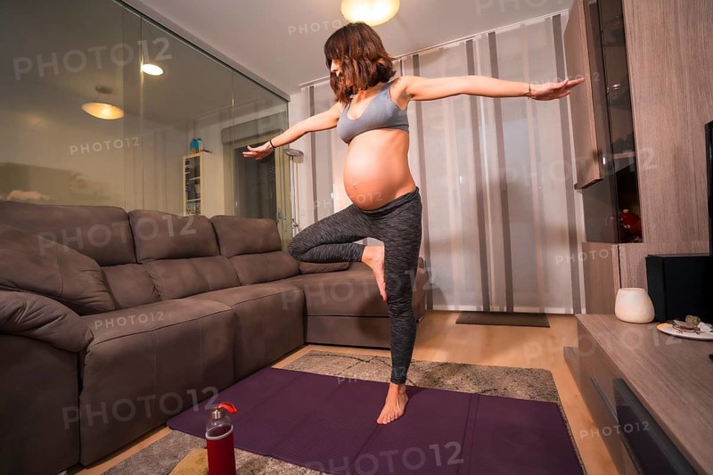 A young pregnant Caucasian woman in a gray t-shirt doing pilates exercise at home. Online exercises in prepartum classes