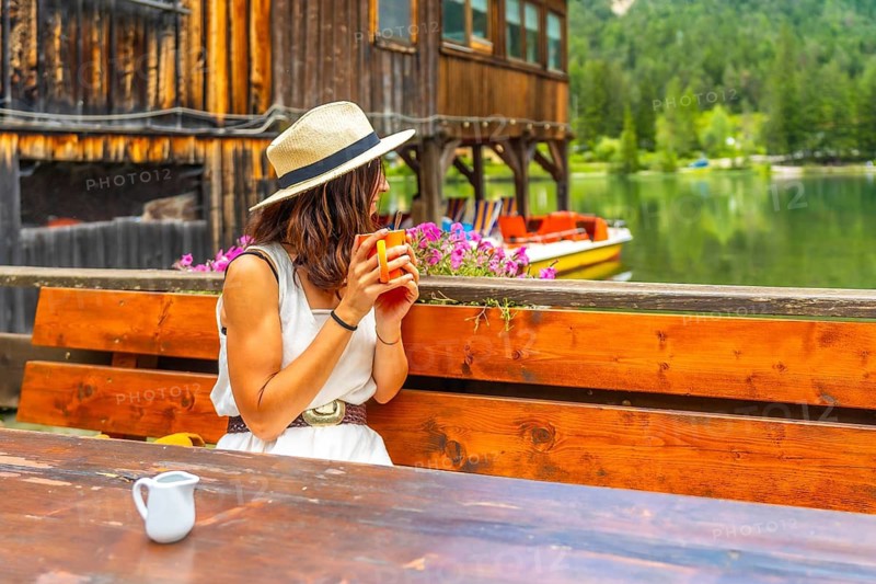 Young woman relaxing with a mug by lake dobbiaco, enjoying the peaceful mountain view in the dolomites