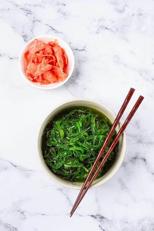 Chuka salad, made from fresh seaweed, with sesame dressing, in a white bowl, with chopsticks and pickled ginger, without people