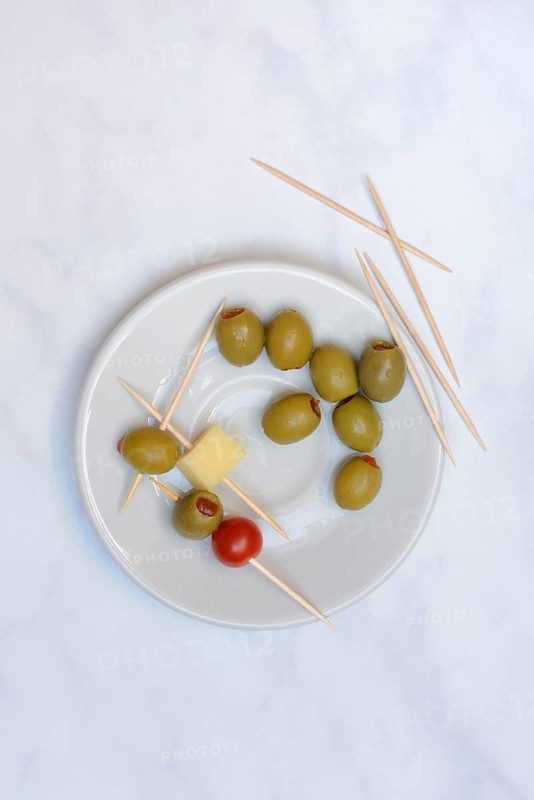 Stuffed olives on plate with cheese cubes and tomato, toothpick