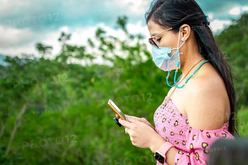 Latin woman with mask checking cell phone outdoors. Cute girl in glasses checking her cell phone