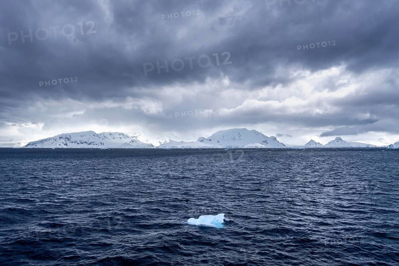 Drifting ice in the dark, moving Southern Ocean against snow-capped mountains under cloudy sky, Antarctic Peninsula, Antarctica