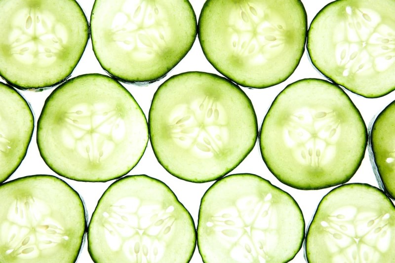 A vibrant pattern of cucumber slices arranged neatly showcases their fresh, green texture on a light background. The translucent flesh and seeds create an inviting, healthy aesthetic