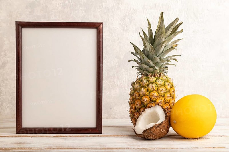 Wooden frame with pineapple, melon, coconut on gray concrete background. Side view, copy space. Tropical, healthy food, vacation, holidays concept