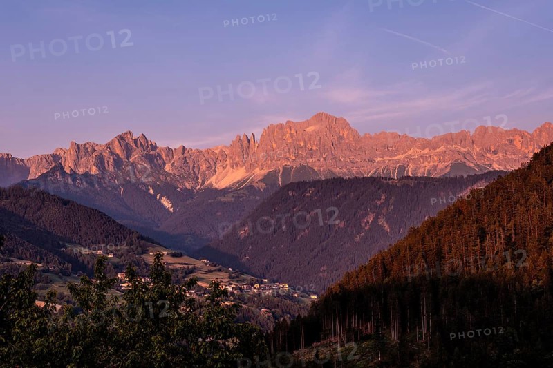 Majestic landscape showing the pale di san martino mountain range glowing pink at sunset over the valley in the dolomites, italy