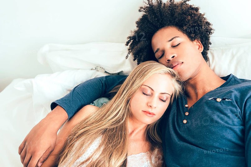A serene image capturing a couple resting peacefully together, embracing while sitting against a white pillow in a cozy home setting. Perfect for themes of love and relaxation