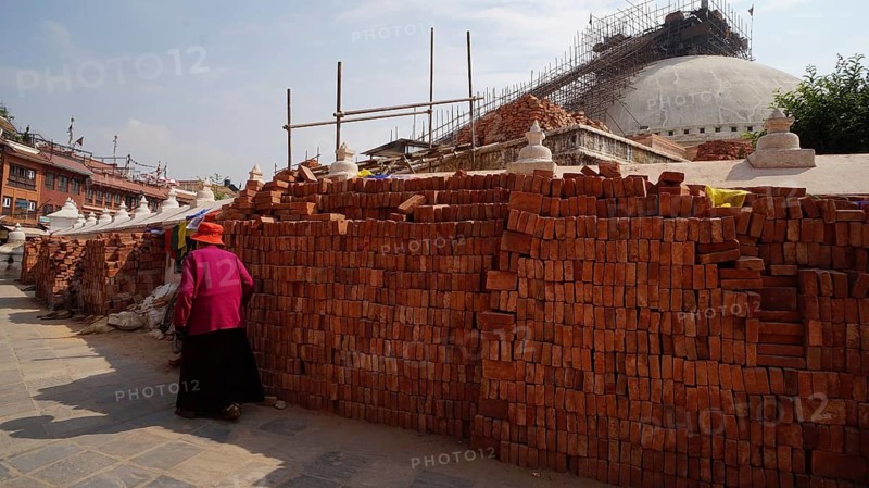 Rebuilding Bodnath after the earthquake, a woman wearing traditional clothes walks past bricks and a construction site, Kathmandu, Nepal