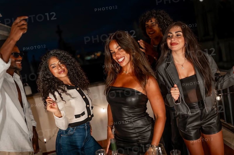 Happy sensual multiracial millennial women dancing together during night party at terrace