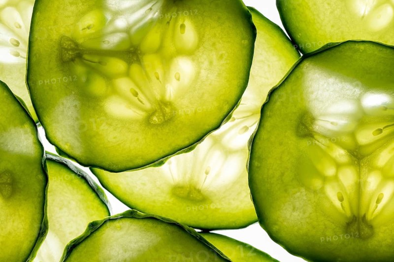 This image features a close up view of translucent cucumber slices, showcasing their vibrant green color and texture, illuminated beautifully by natural light