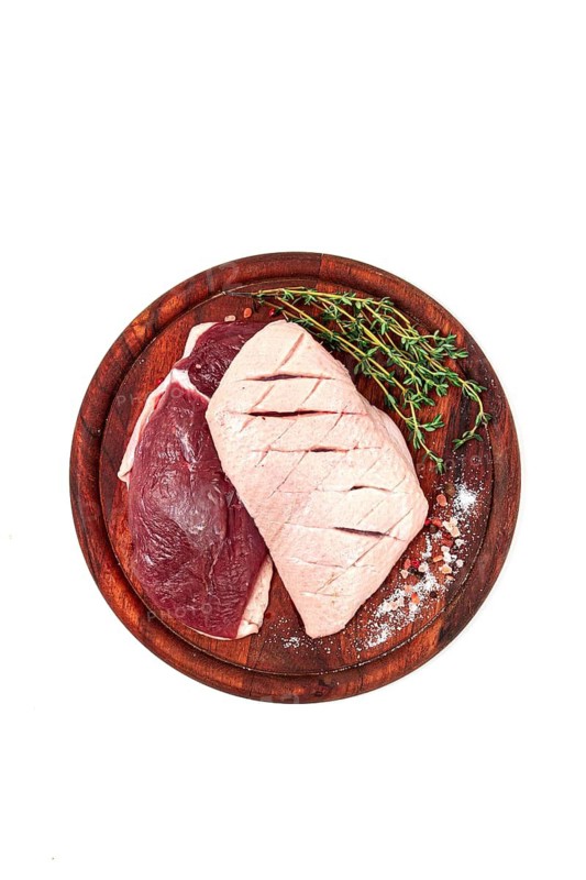 Fresh raw duck breasts, on a wooden chopping board, with herbs and spices, on a white background, no people