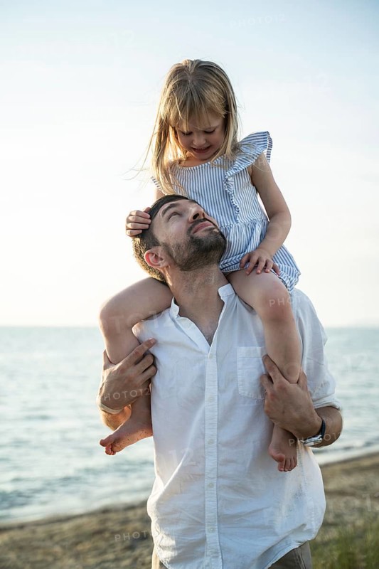 A loving father carries his smiling daughter on his shoulders during a warm summer day in Italy. They enjoy a joyful and carefree moment together in nature, creating cherished memories