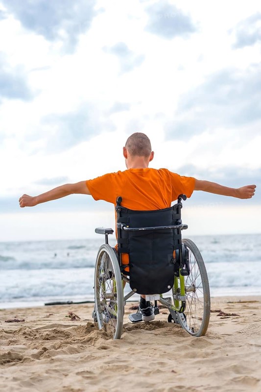 A disabled person on his back in a wheelchair on the beach feeling free