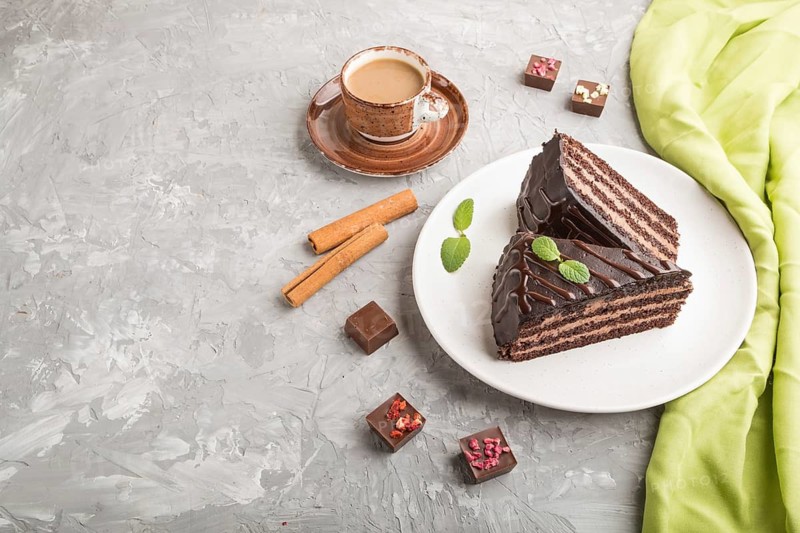 Homemade chocolate cake with milk cream and a cup of coffee on a gray concrete background with green textile. side view, copy space