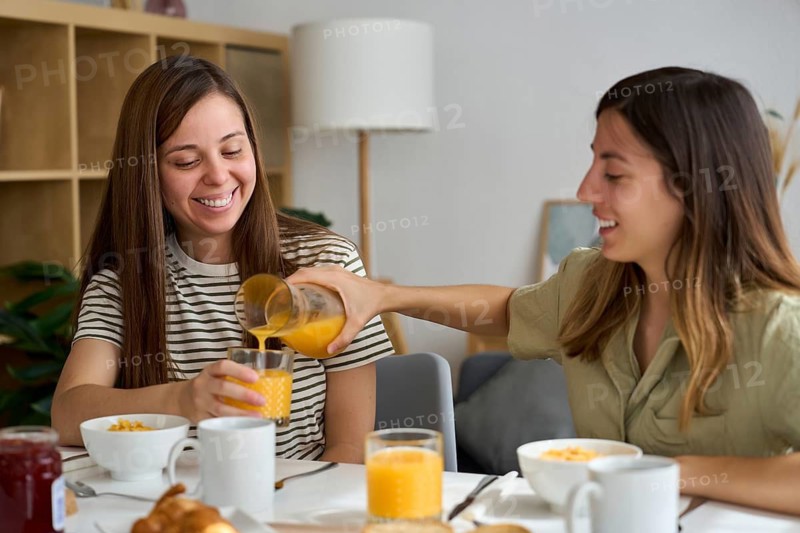 A happy lesbian couple shares a breakfast at home, enjoying each other's company Orange juice, croissants, and laughter create a cheerful, intimate moment