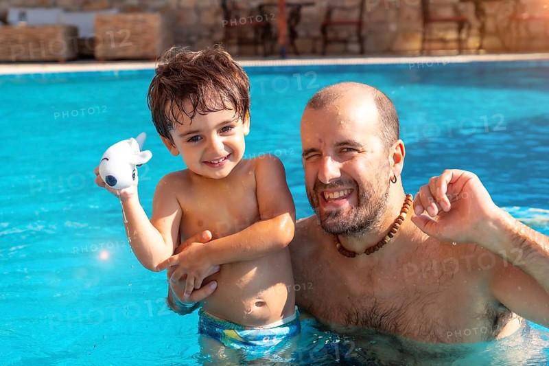 Portrait of father and son in swimming pool in summer playing enjoying and smiling on vacation