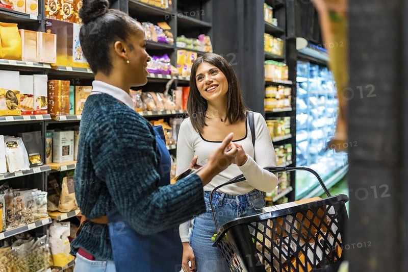 Smiling saleswoman advising customer choosing groceries in supermarket with organic and healthy products