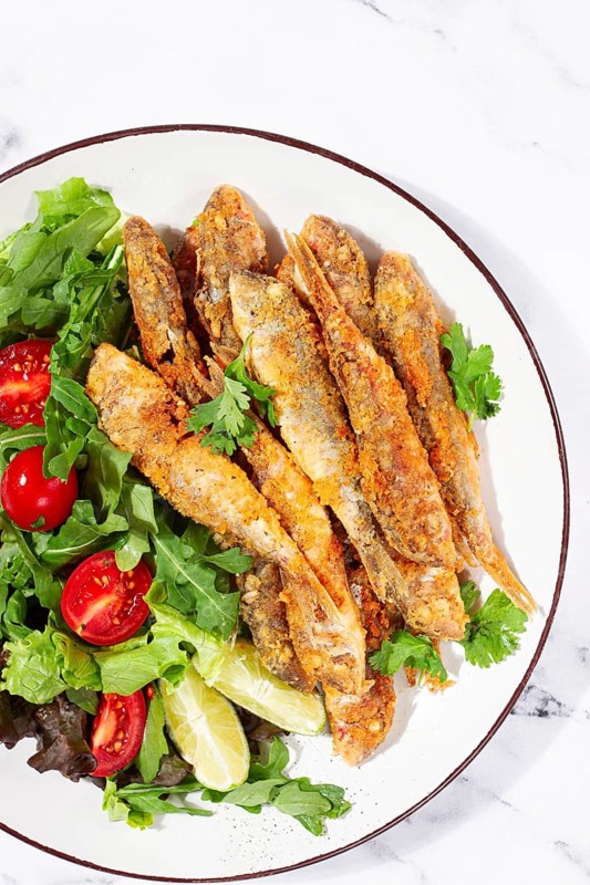 Fried crispy mullet fish, with fresh salad, on a plate with lime, no people