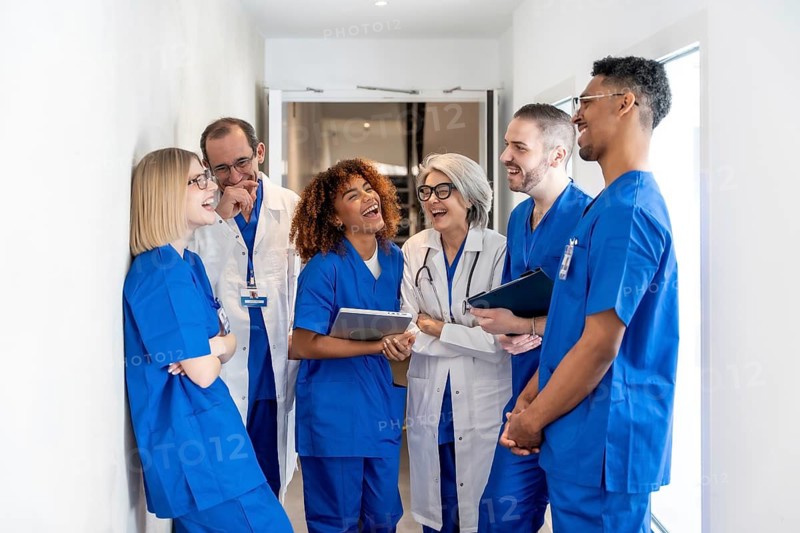 Healthcare professionals from various backgrounds smiling and laughing together during a break in a modern clinic corridor, symbolizing teamwork, joy, and a positive work environment