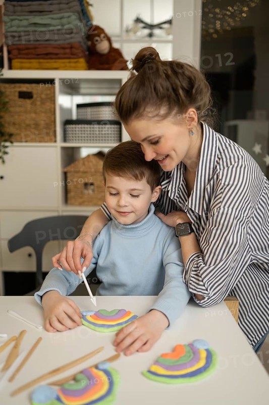A caring adult guides a child in a creative art lesson, using modeling clay to create colorful rainbows. The warm setting enhances creativity and learning in a fun environment