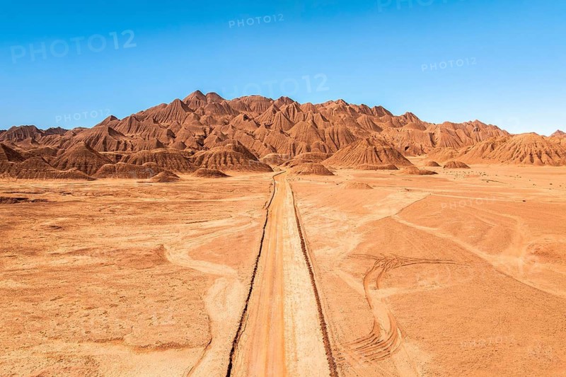 A solitary dirt road stretches through a vast, arid desert landscape leading towards striking, rugged mountains under a clear blue sky in the argentine Puna, capturing a sense of solitude