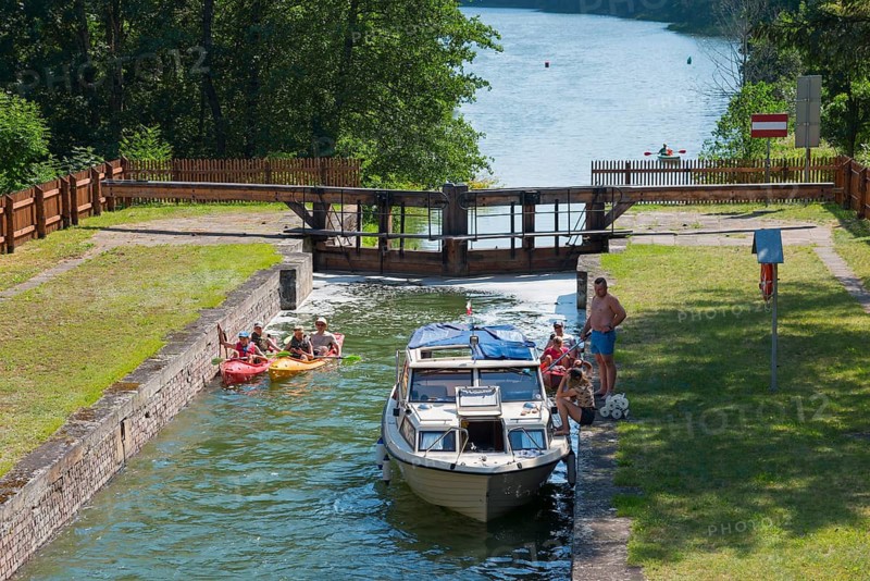 A boat and canoes travelling on a river through the lock, surrounded by green nature, Sluza Paniewo, lock between the lakes Paniewo and Krzywe, Plaska, Powiat Augustowski, Podlaskie Voivodeship, Poland